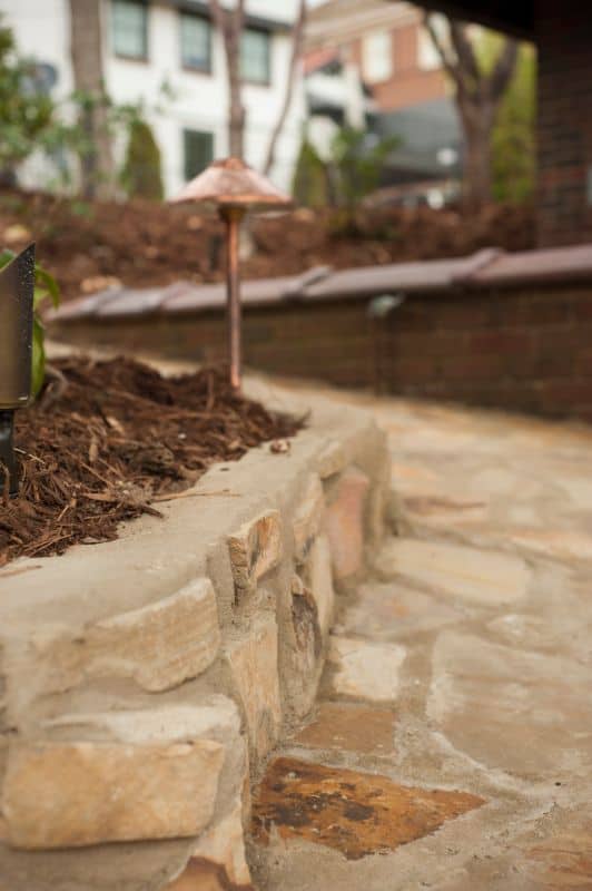 Natural stone retaining wall with mulch and pathway landscaping, designed by John Russell Landscape Architect.