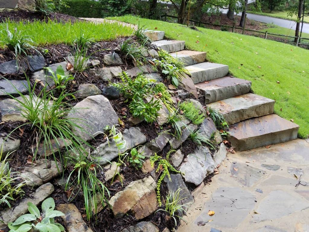 Natural stone retaining wall with lush plants and landscaped garden, showcasing expert landscape design and sustainable outdoor spaces.