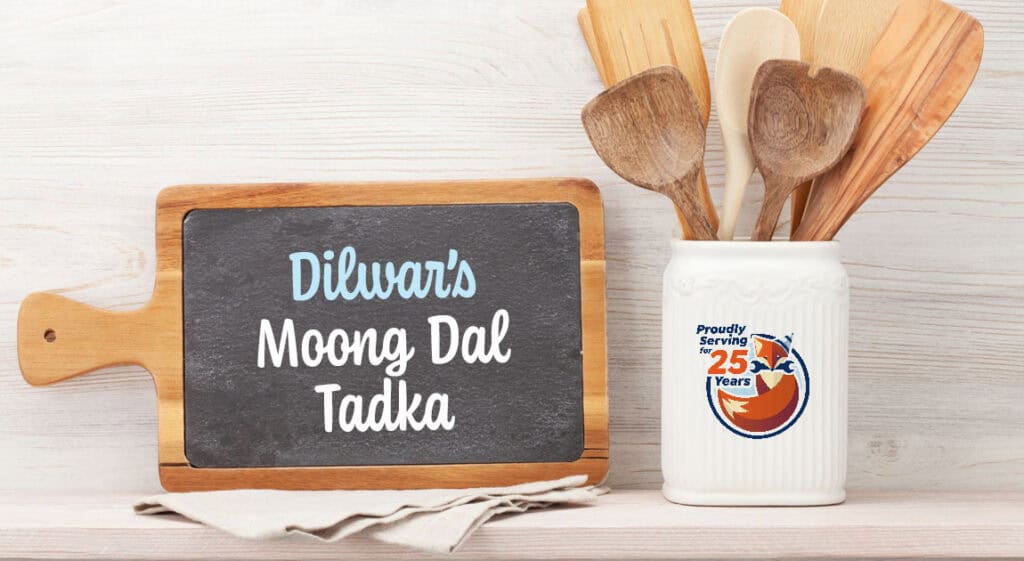A chalkboard sign reads "Dilwar's Moong Dal Tadka"—a classic Indian Lentil Curry—next to a white container of wooden utensils. The container displays a "Proudly Serving 25 Years" logo.