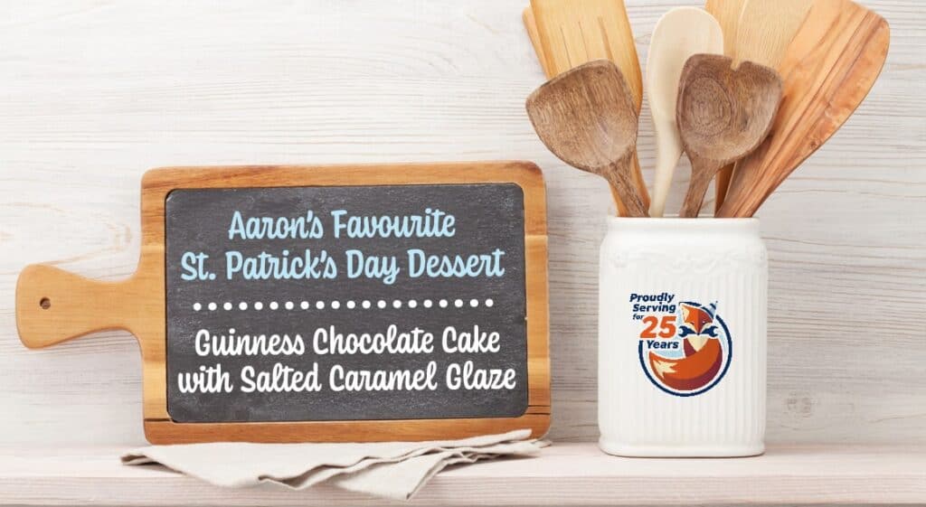 A chalkboard on a cutting board displays "Guinness chocolate cake"; next to it is a ceramic container holding wooden utensils and a "25 years" logo, hinting at a celebration-worthy dessert with decadent salted caramel glaze.