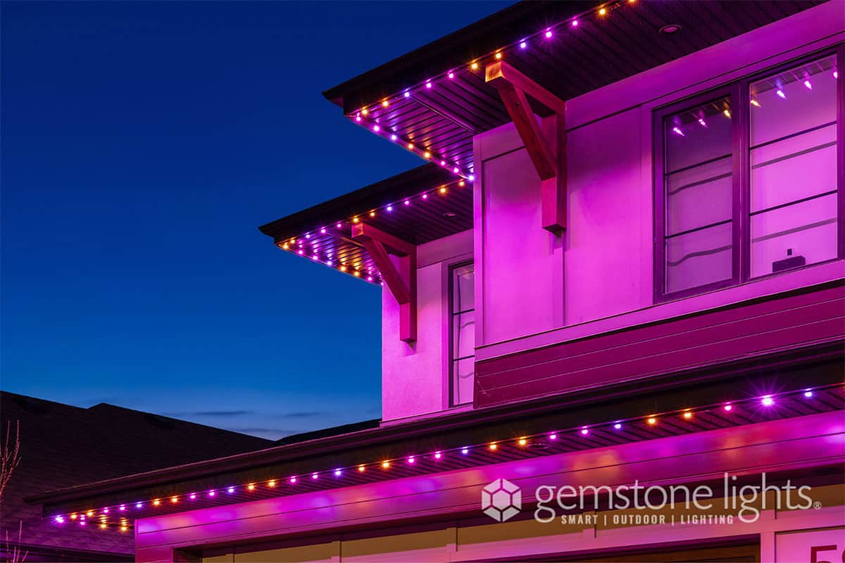 A modern house at dusk with purple and orange LED lights along the roofline, showcasing Gemstone Lights outdoor lighting. Learn more about us and how we can transform your home with stunning, customizable illumination.