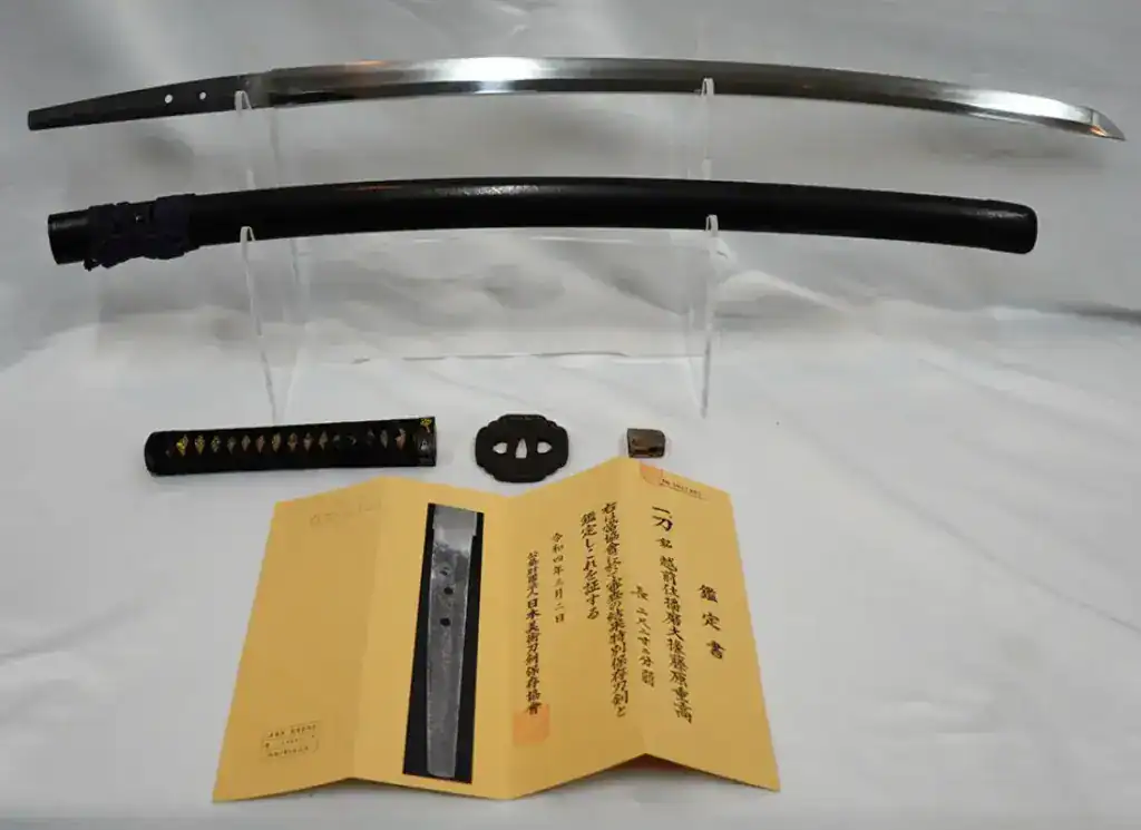 Katana with scabbard, fittings, and authentication papers displayed on stand