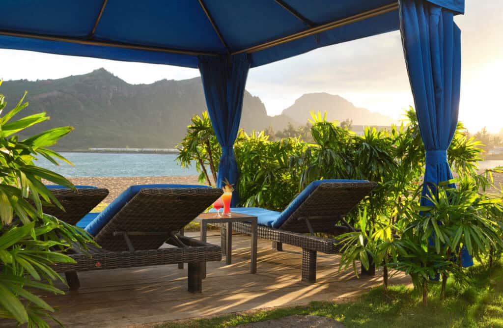 A blue gazebo with two lounge chairs overlooks the ocean in Kauai, Hawaii, creating a serene coastal retreat. Gallery Image