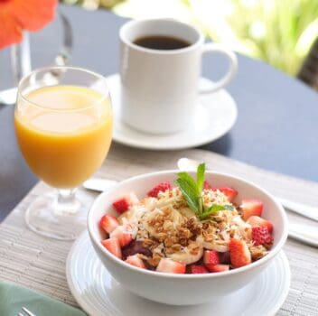 A cozy beach breakfast scene with a spread of fruits, pastries, and coffee, overlooking the sandy shore.