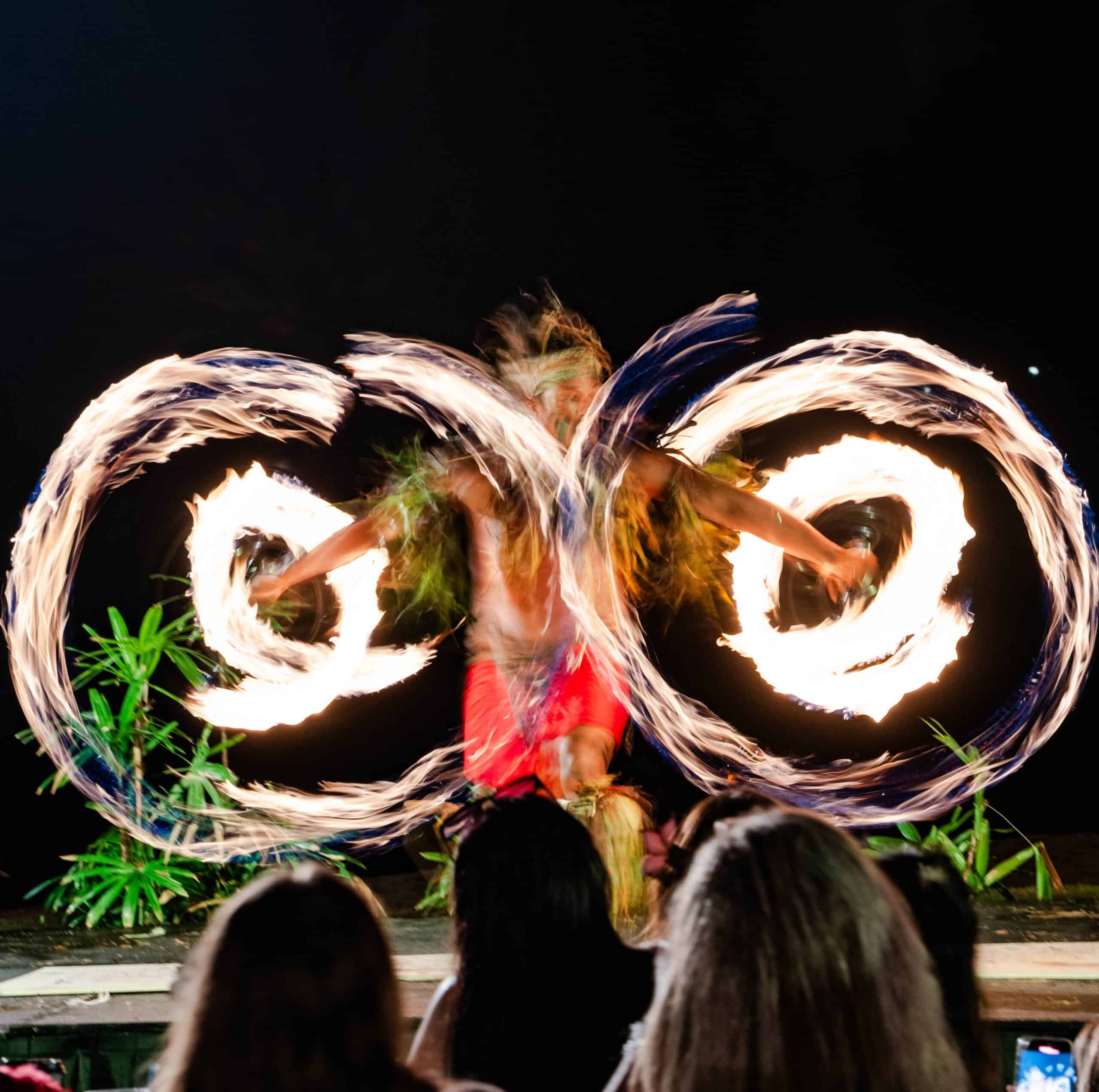 A performer spins glowing fire rings at night, creating a mesmerizing display of light and movement against the dark sky.