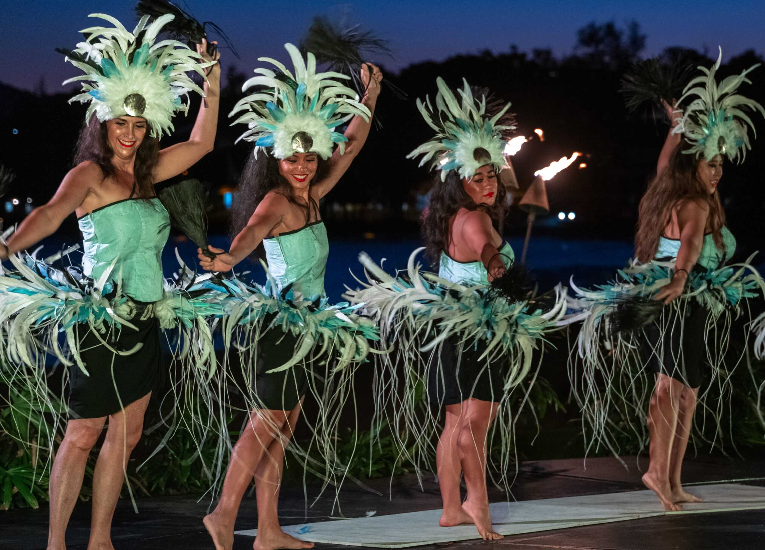 A night scene featuring dancers in green costumes, gracefully performing with a backdrop of darkness and subtle lighting.