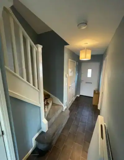 Hallway interior with staircase, front door, and modern lighting fixtures.