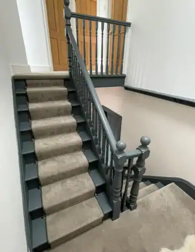 Staircase with carpet runner, wooden handrail, and decorative newel posts in a home.