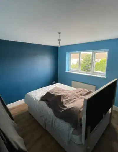 Blue painted bedroom with a large window and minimal decor, showcasing a recent interior painting pr.
