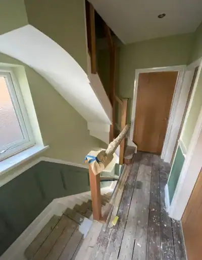 Staircase under renovation with protective covering on the newel post, in a home with green walls an.