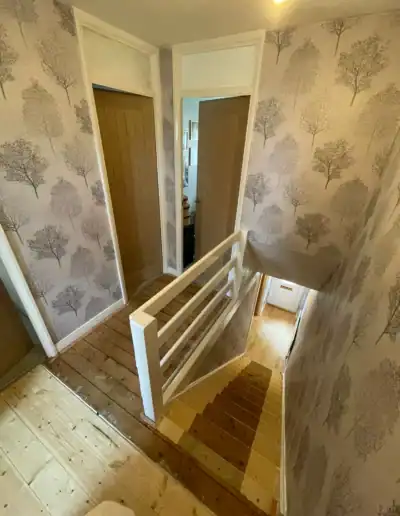 Interior view of a staircase with patterned wallpaper and wooden steps in a home.