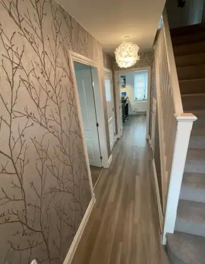 Hallway with stylish tree-patterned wallpaper, wooden flooring, and contemporary lighting.