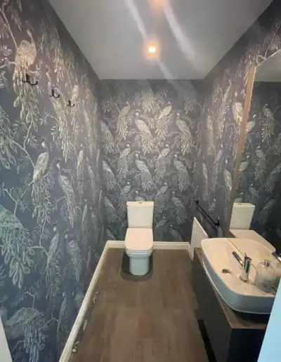 Botanical wallpaper bathroom featuring a toilet and sink with contemporary design and stylish decor.