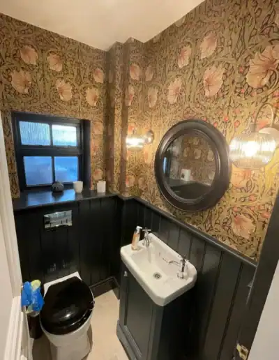 Vintage bathroom with floral wallpaper, black wainscoting, and modern fixtures.