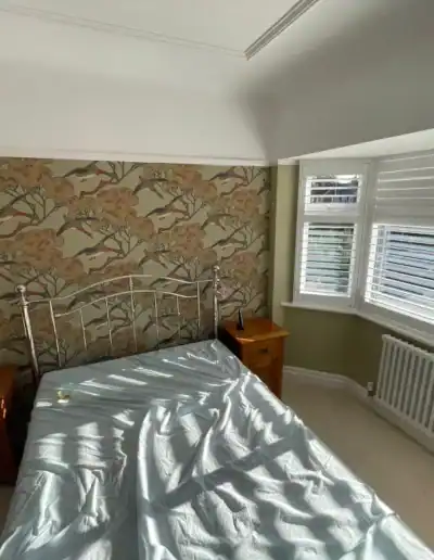 Bright bedroom featuring floral wallpaper, white window blinds, and a cozy bed setup.