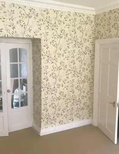 Elegant floral wallpaper in a living room with white doors and beige flooring.