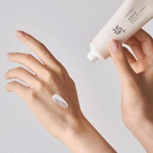 Hand trägt Sonnencreme auf das Gesicht auf, mit Sonnenschutzcreme in der Hand.