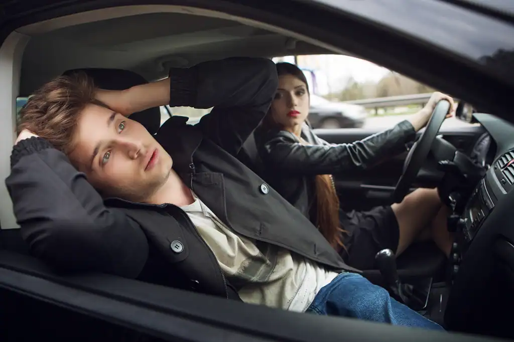 Young couple sitting inside a car, looking frustrated after a roadside incident, possibly involving legal issues. Focus on representing legal assistance for car accidents and personal injury cases at The Law Office of Benjamin Arnold.