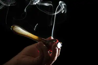 A hand holding a lit joint with smoke rising, set against a black background, representing issues related to drug use and legal concerns.