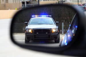 Police car with flashing lights seen through a vehicle's side mirror in a parking lot.