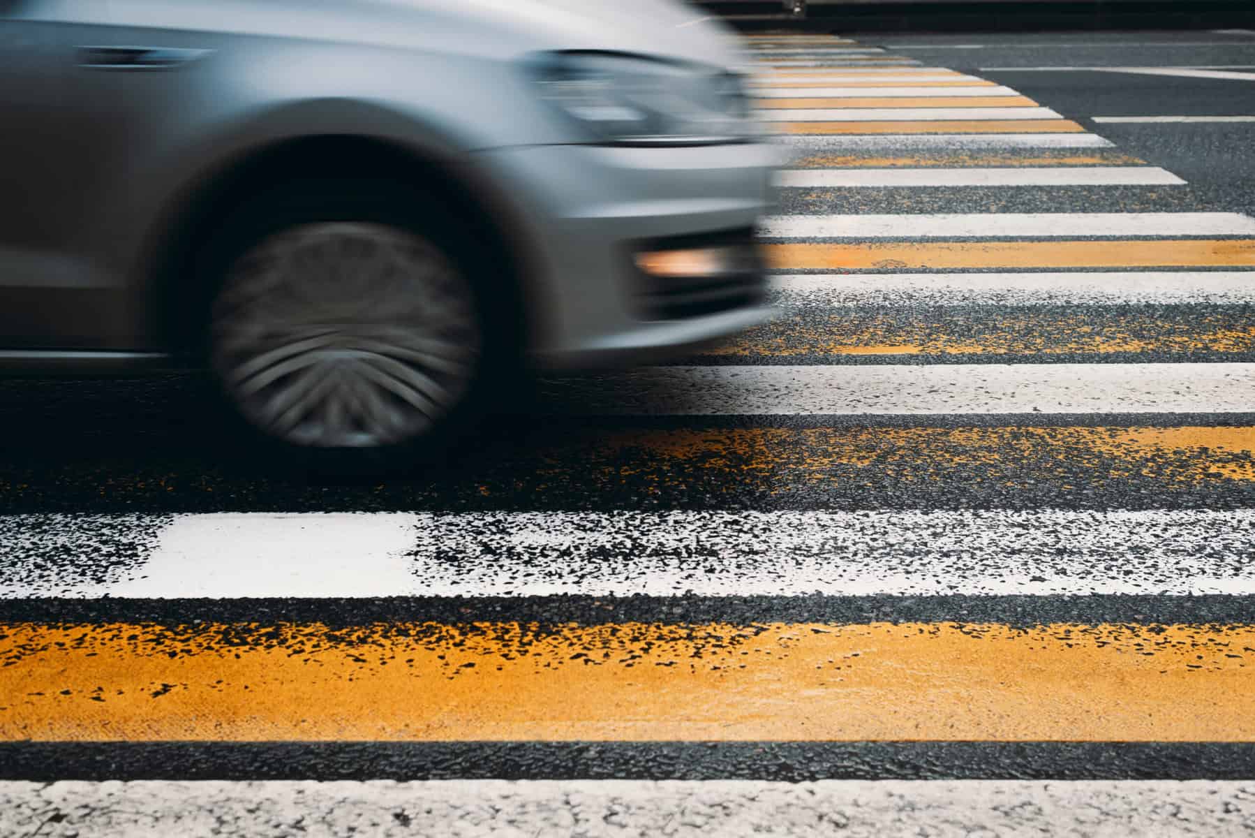 Foot of a moving car crossing a pedestrian crosswalk on a busy street, emphasizing traffic accident and personal injury legal services.