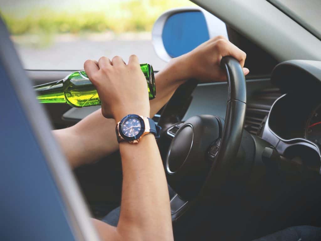 Bottle of alcohol in hand near steering wheel, dangerous driving behavior, vehicle interior, potential DUI concern, legal issues, law office of Benjamin Arnold, Kansas City DUI attorney, drunk driving legal help, car journey, alcohol consumption.