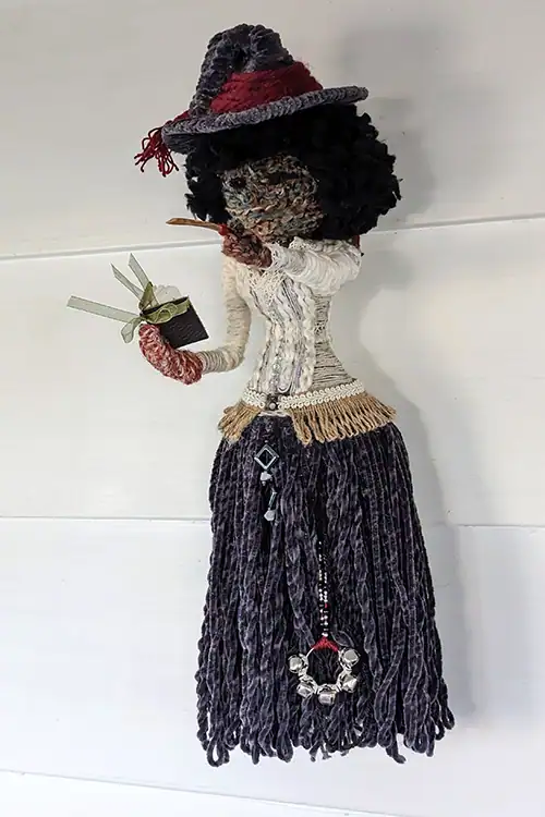 Hannah the Kitchen Witch wearing her hat, holding a recipe book, and revealing witch's bells under her skirt.