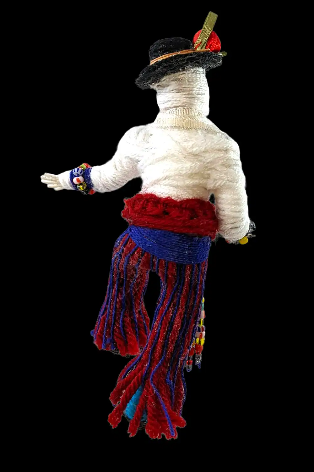 Rear view of a handcrafted male Day of the Dead skeleton doll, showcasing his detailed attire with a black hat and vibrant red and blue pants.