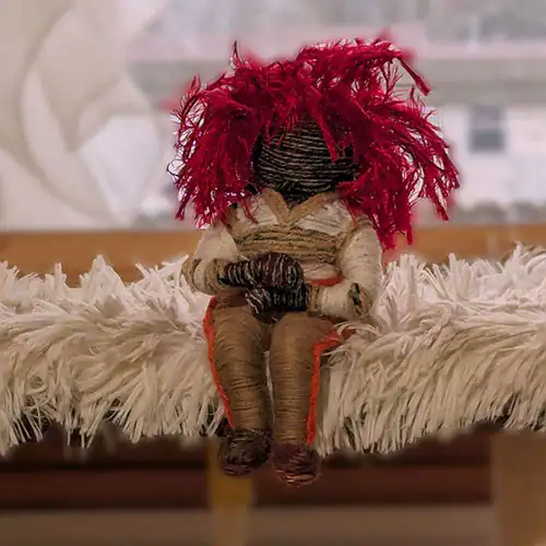 Voodoo art doll with red hair in a tracksuit with orange stripes on the legs and a V-neck long-sleeve top.