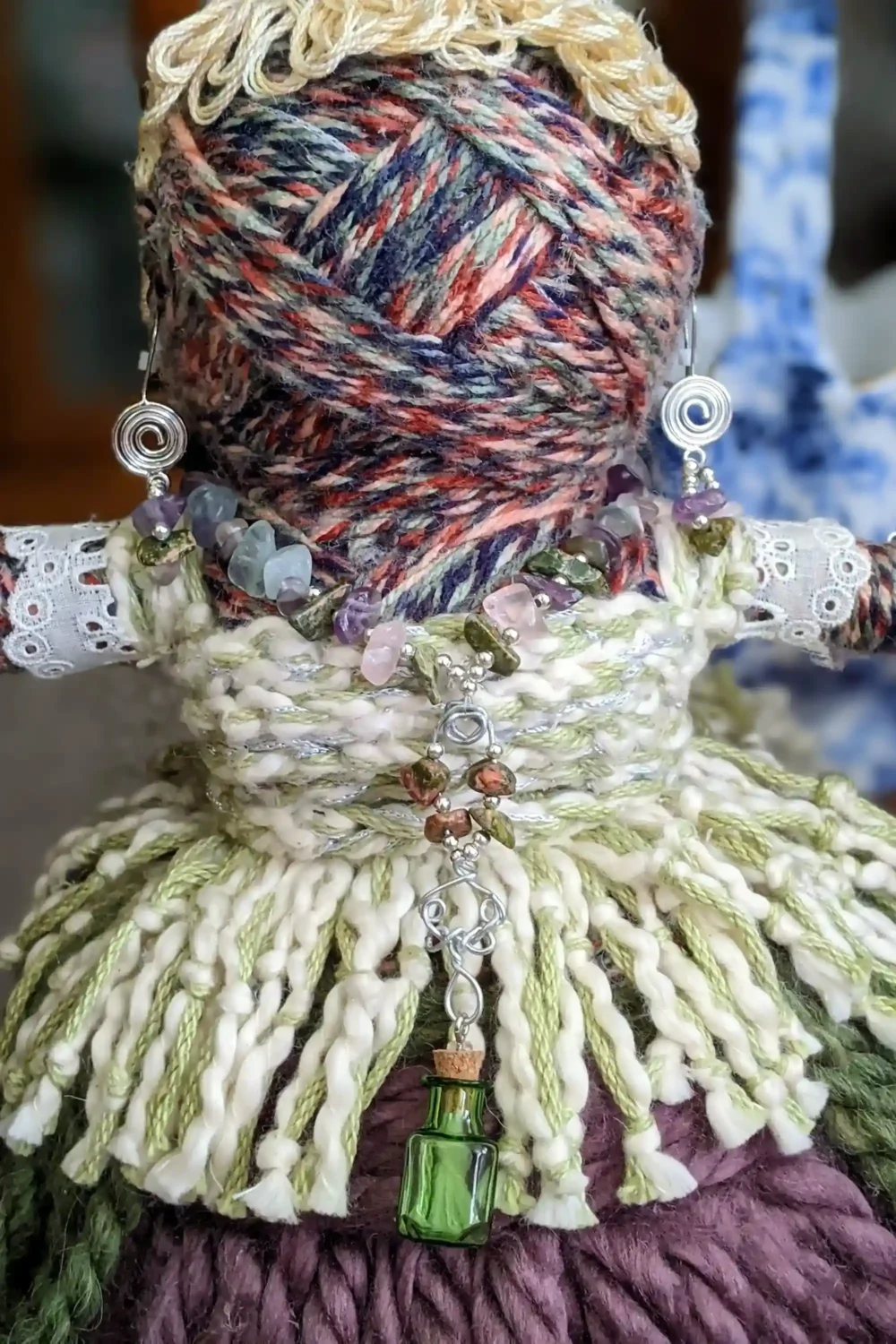 Close-up of Leela the health and wellness art doll from head to hips, showcasing her gemstone jewelry and a small green bottle pendant for jasmine aromatherapy oil.