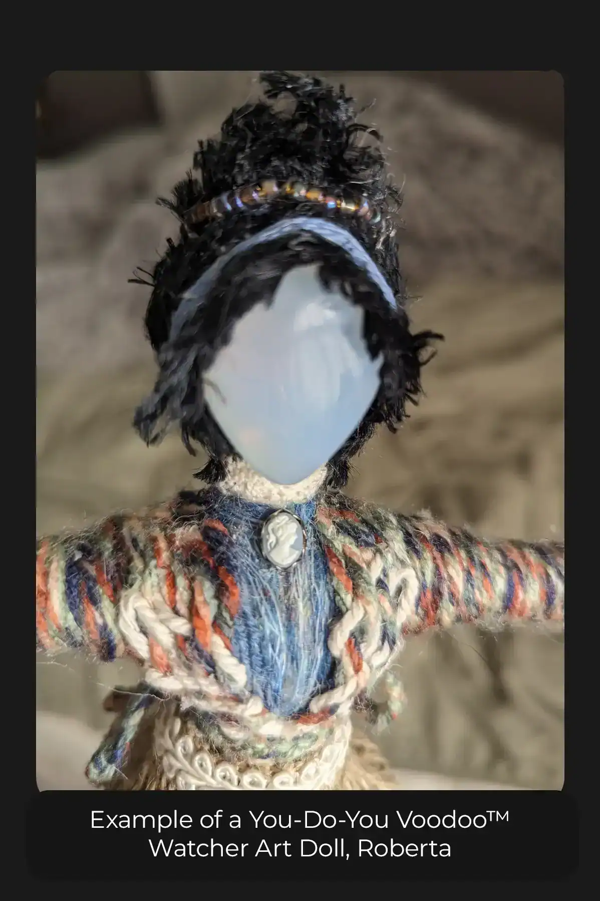 Watcher art doll with moonstone head, a cameo at her throat, open jacket and blue and beaded decorations in her black hair.