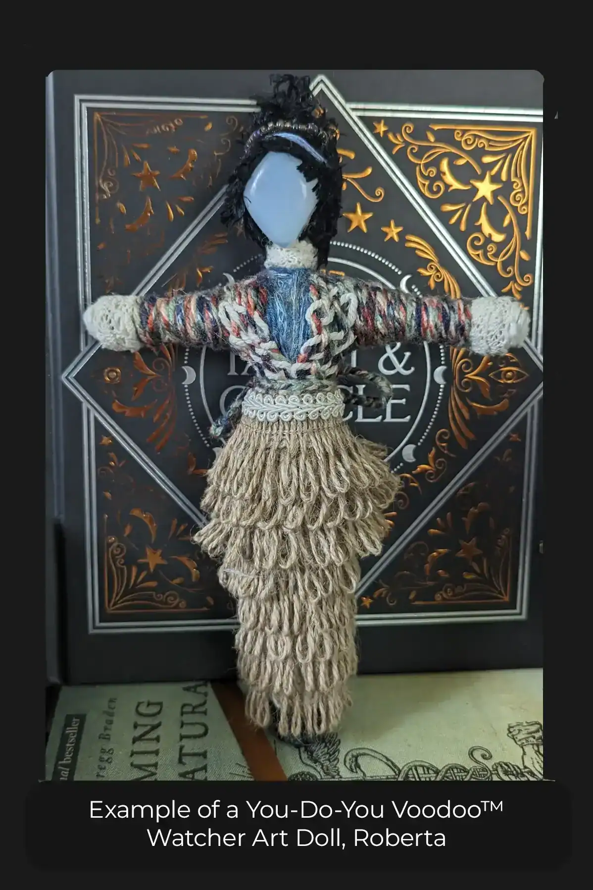 A Watcher art doll standing on a book in front of a book. She's about 7 inches tall, twine ribbon skirt, black messy hair.
