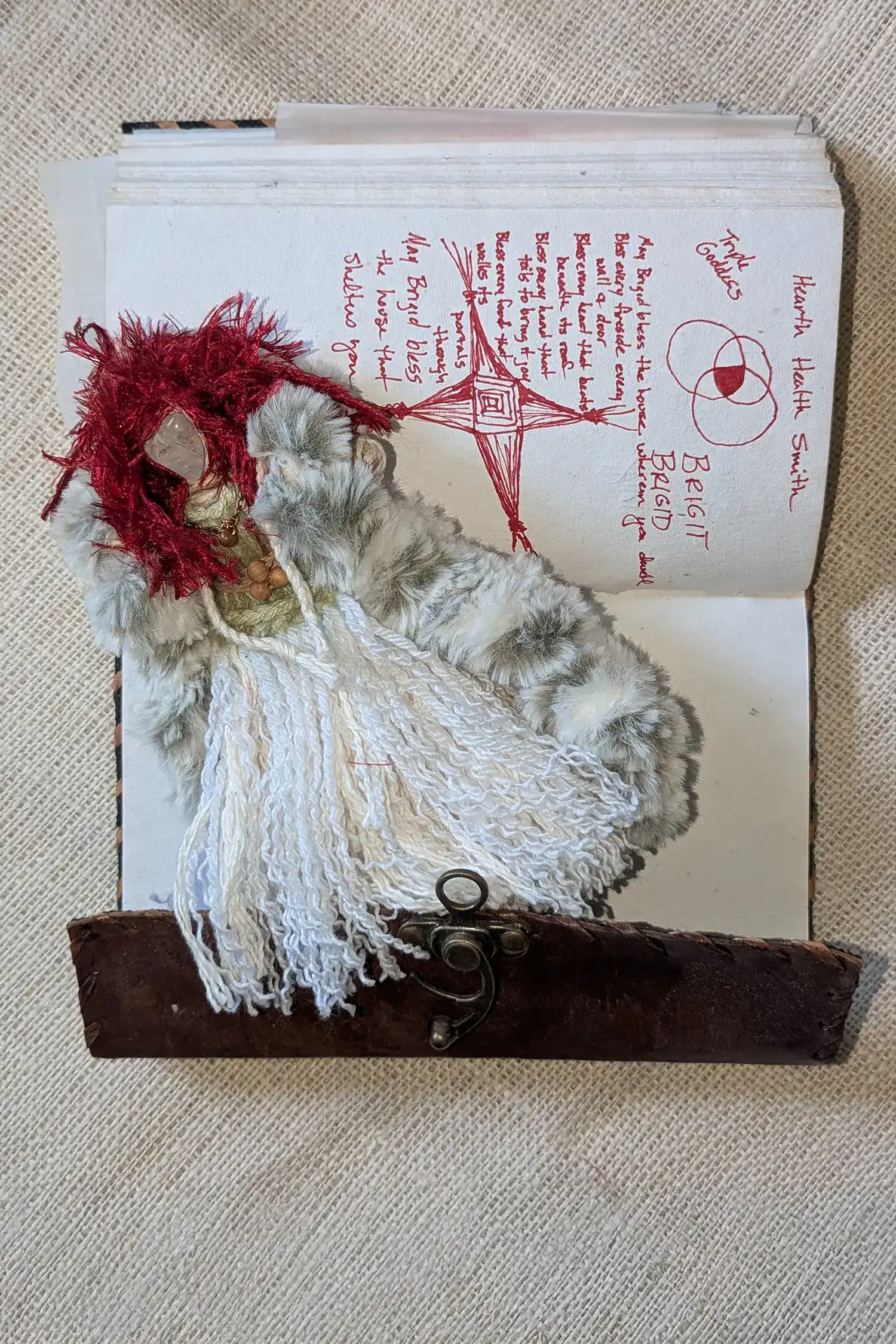 Brigit, a You-Do-You Voodoo™ art doll, lies on a journal page with some of her symbols and a blessing on it.
