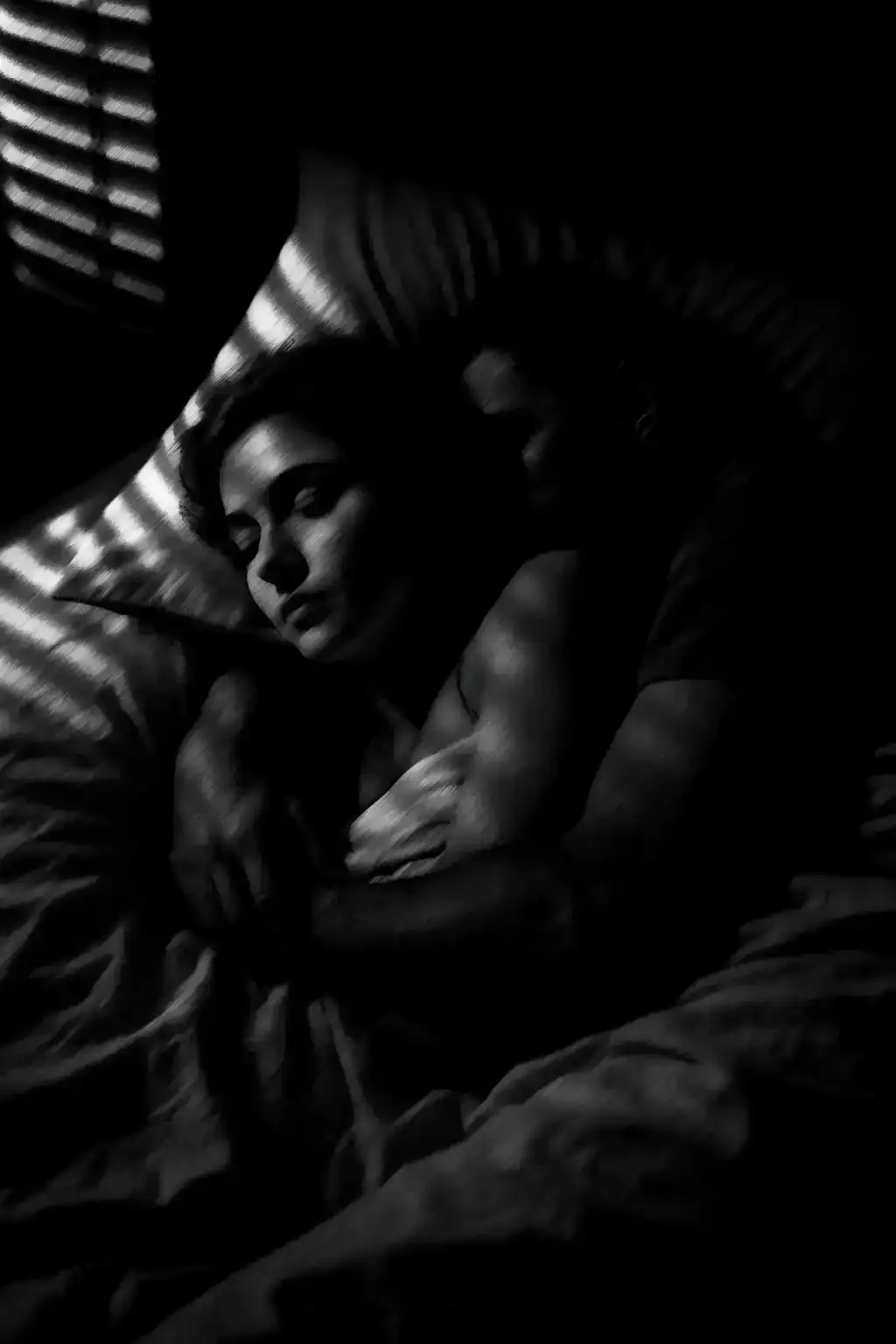 Dark portrait of woman sleeping with shadows and light patterns, black and white image.