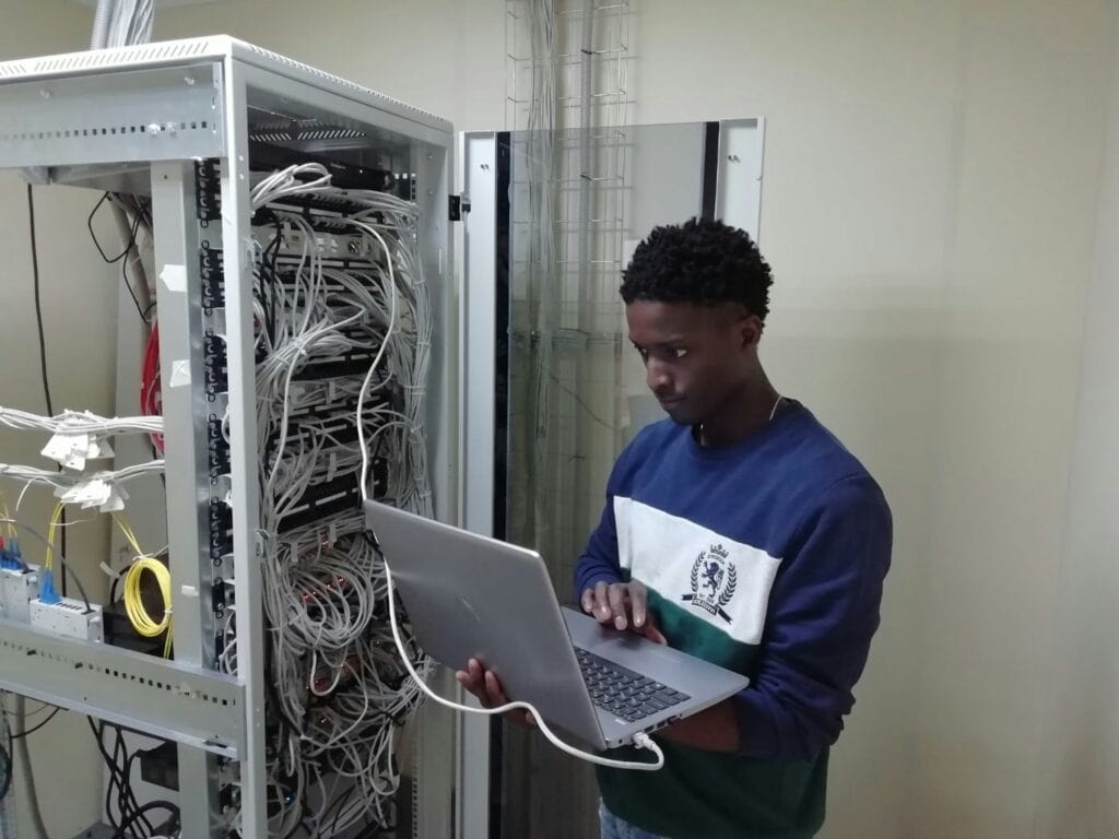 Cabled server rack setup with technician using a laptop for network management or troubleshooting.