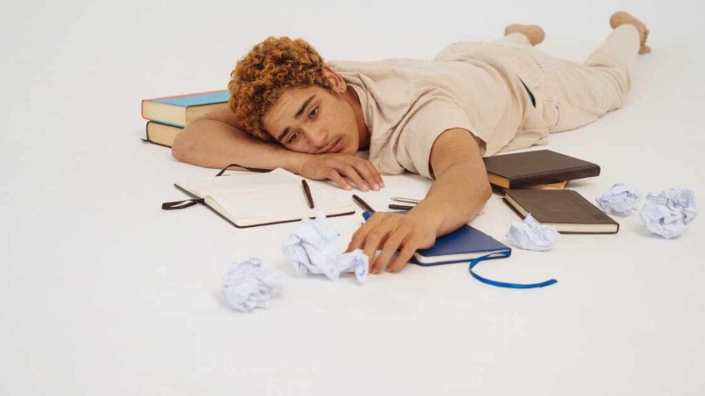 Teen lying on floor overwhelmed by books and papers, illustrating emotional exhaustion tied to teen depression myths.