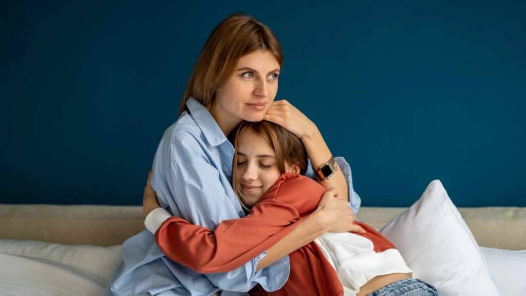 Mother hugging her teen daughter on a couch, offering comfort and emotional support during a difficult moment.