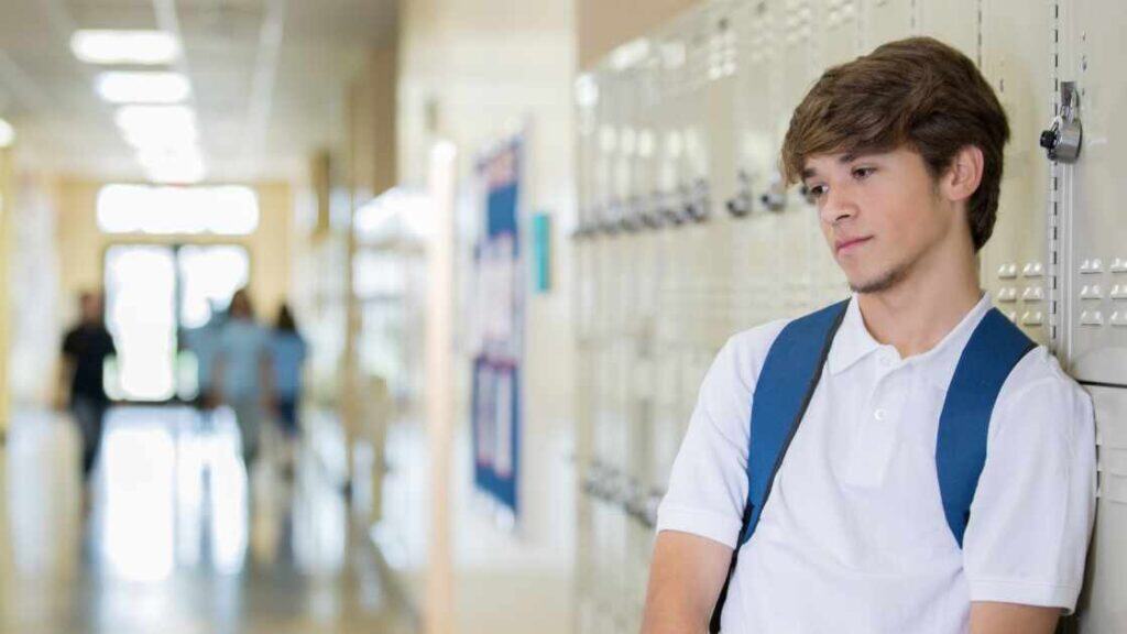 Teen boy leaning against school lockers looking sad, representing signs that may distinguish depression from typical moodiness.