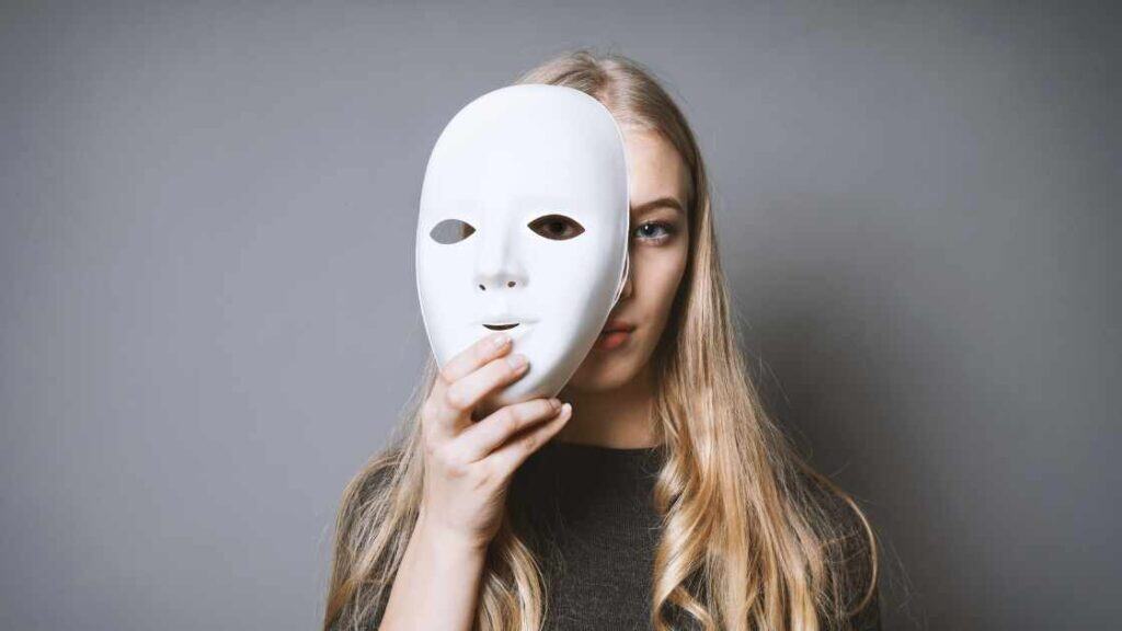 Teen girl holding a white mask in front of her face, symbolizing the hidden struggle between moodiness and clinical depression.