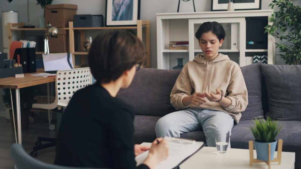 Teen boy in therapy session at a residential treatment center, expressing emotions with hands, counselor taking notes.