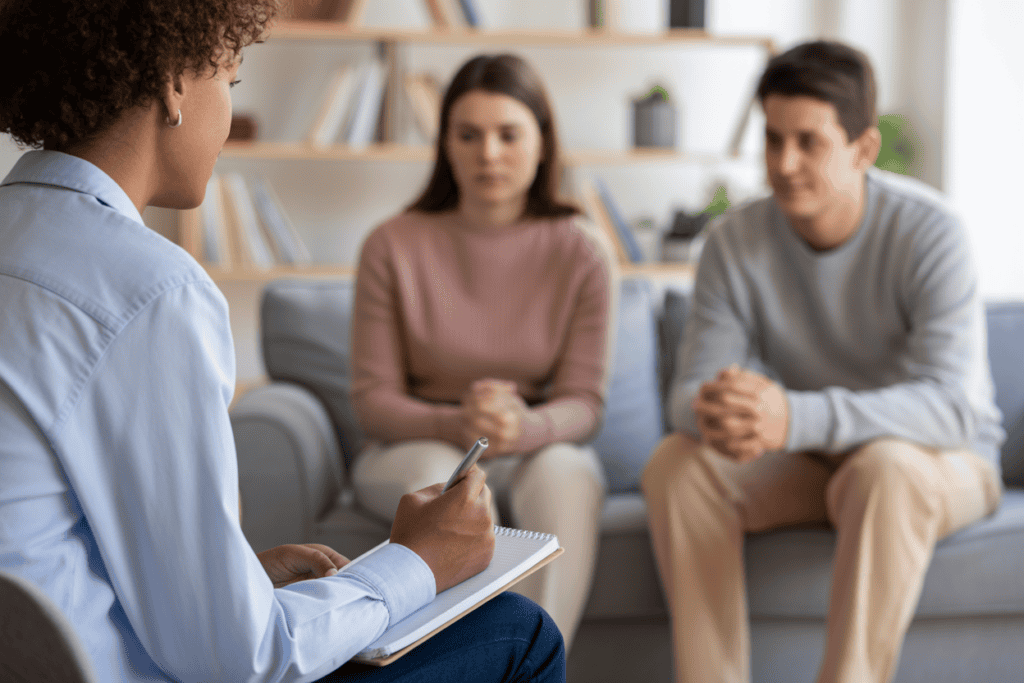 A compassionate mental health professional listens intently to a teen and their parent in a warm, welcoming office setting.