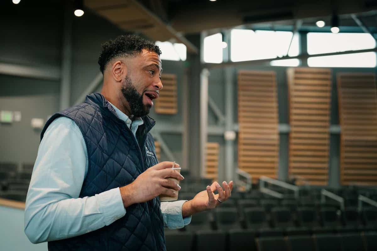 A man with a coffee standing in a church auditorium talking to someone out of frame