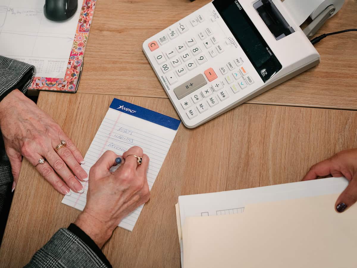 Someone writing on a notepad with a calculator nearby