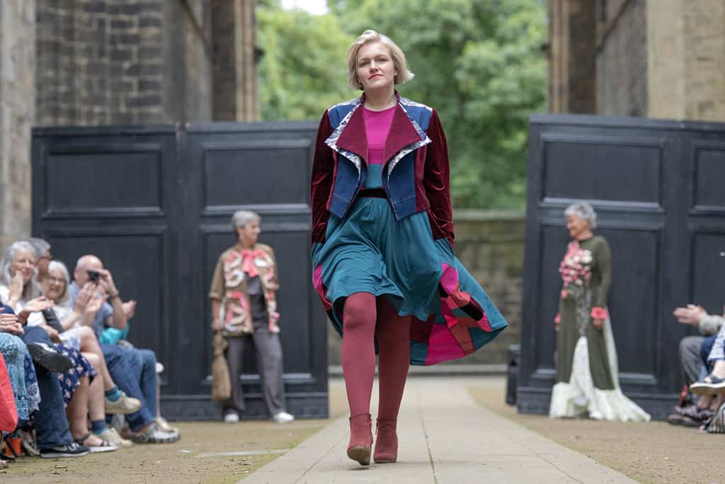 A model wearing a brightly coloured top and skirt, with a velvet and denim jacket.