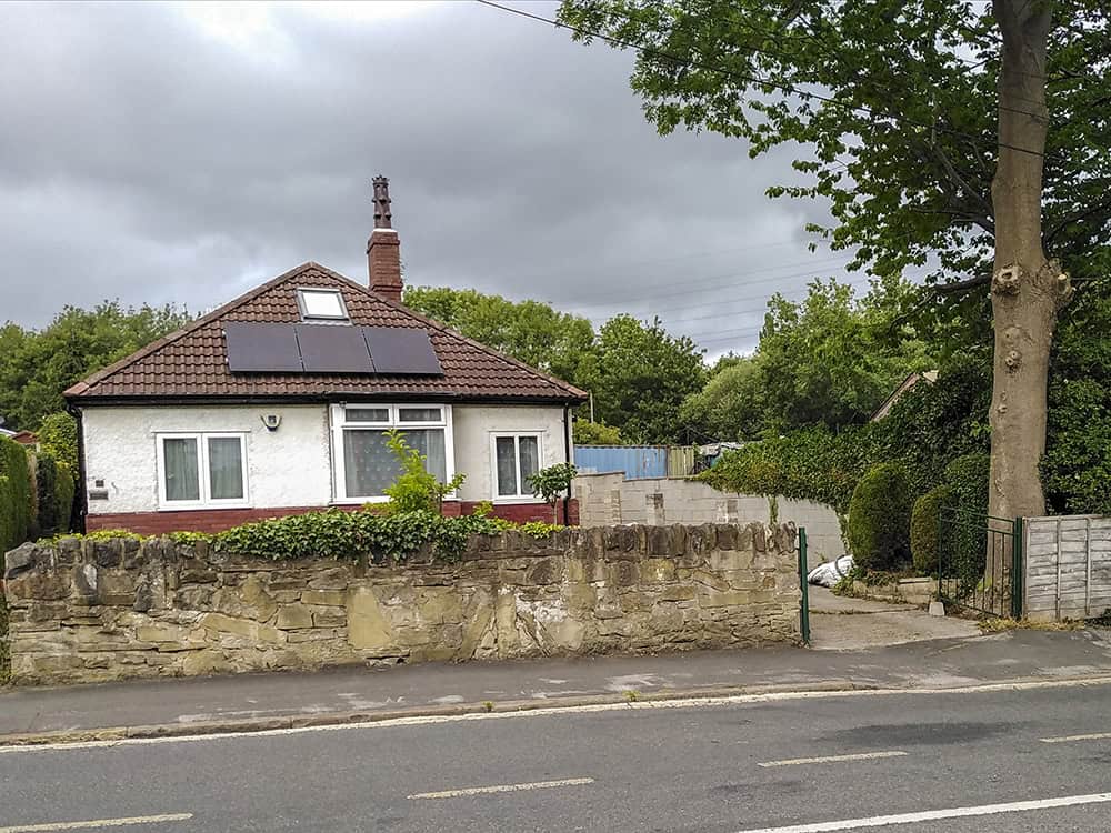 The exterior of 14 Vesper Road, shown from the road. It is a bungalow with white walls and a red tiled roof with solar panels. There is a stone boundary wall, and a concrete driveway.