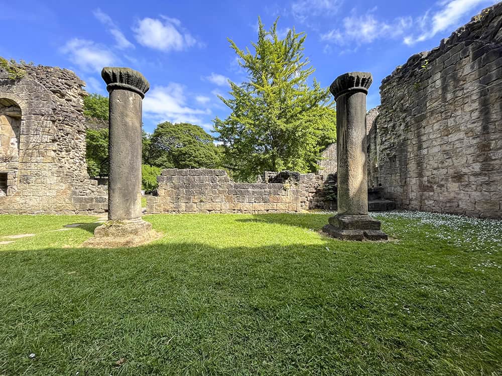 Exterior of Kirkstall Abbey Infirmary ruins, with two stone columns surrounded by grass.