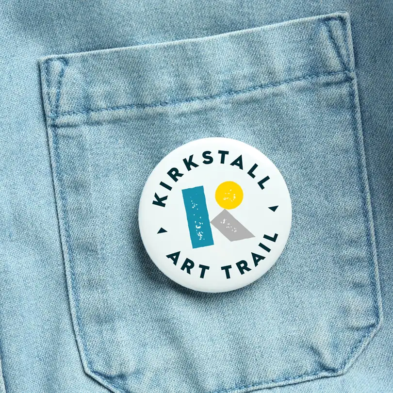 a white badge with the new Kirkstall Art Trail logo pinned to a jacket pocket