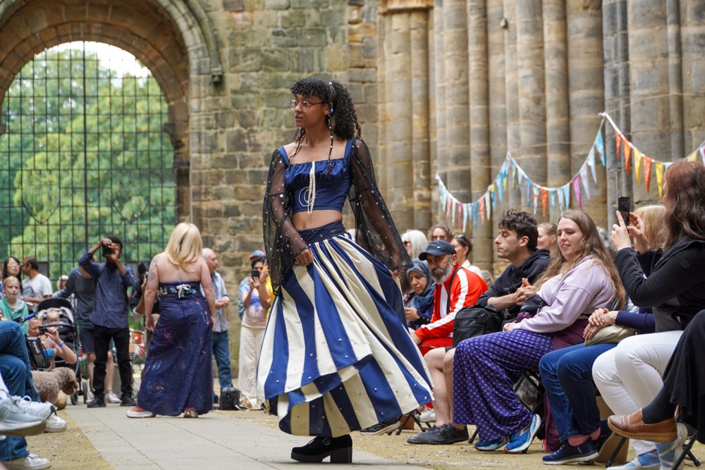 A model walks the catwalk in a navy crop top with sheer bell sleeves and a voluminous blue-and-cream striped skirt.