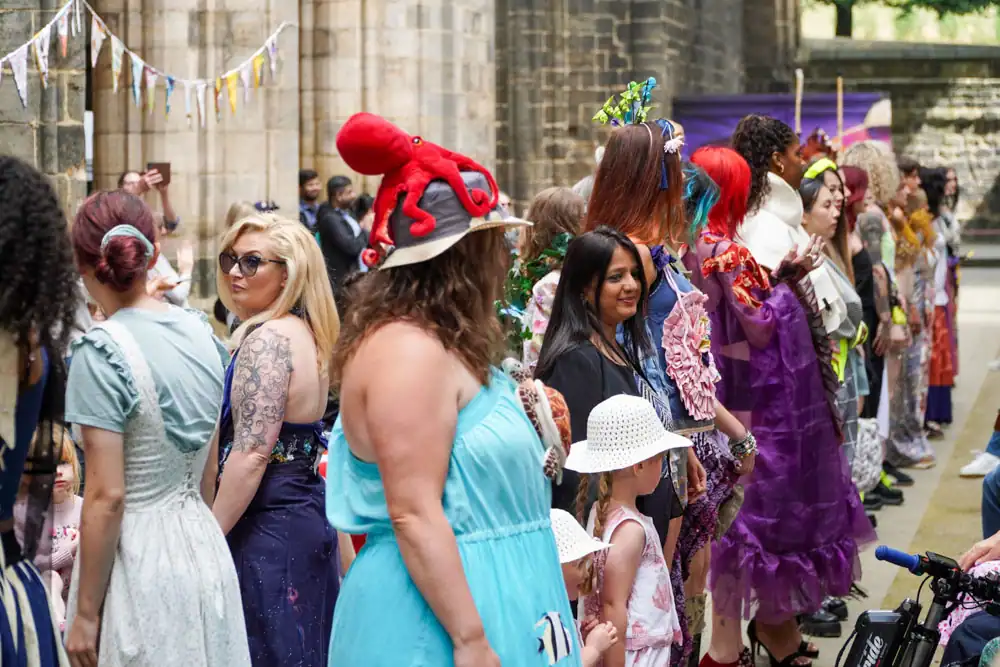 A line of models in varied outfits pose on the catwalk, one wearing a hat topped with a red toy octopus.