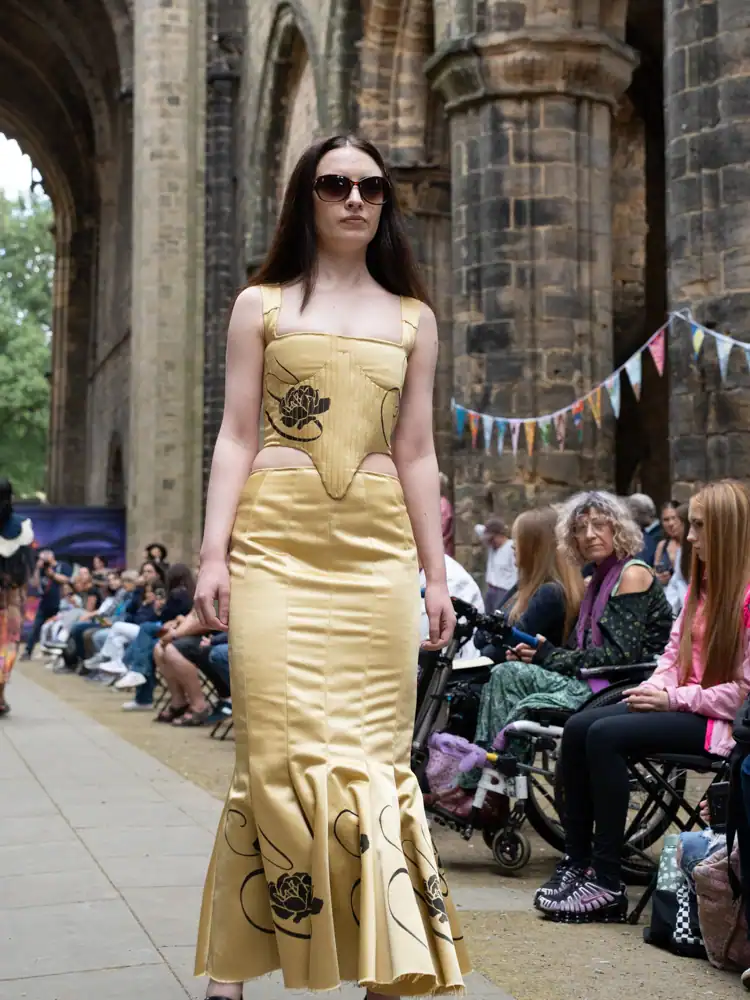 A model walks the catwalk in a pale gold corset dress with black floral print and a mermaid-hem skirt.